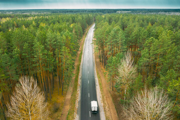Aerial View Of Highway Road Through Spring Forest Landscape. Top View Of Truck Tractor Unit Prime Mover Traction Unit In Motion On Freeway. Business Transportation, Trucking Industry