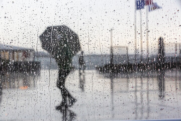 Selective focus shot of a wet window with a view of people with umbrella walking on a rainy day