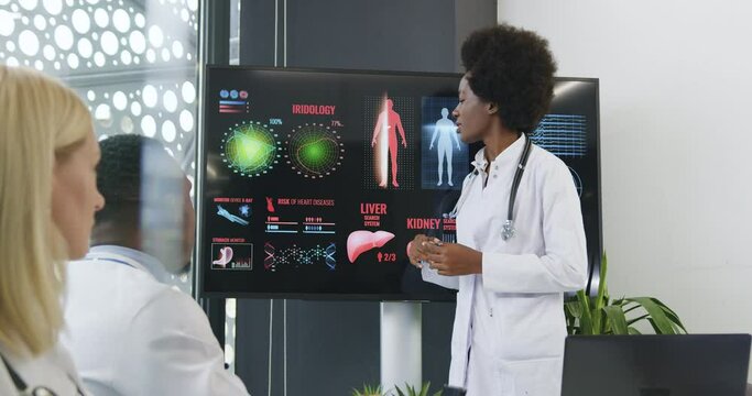 Adorable black successful wise female doctor reporting about heart deseases during seminar in front of high-skilled serious diverse medical coworkers using presentation on digital monitor