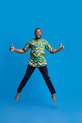 Fototapeta na wymiar Happy black guy jumping up over blue background