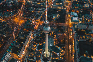 Berlin, Deutschland Alexanderplatz Fernsehturm nach Sonnenuntergang in der Abenddämmerung mit wunderschön beleuchteten Straßen in orangefarbenen Lichtern eines Großstadt-Stadtbildes, Luftaufnahme