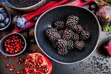 Purple raw vegetables and fruits on black background and blackberries on a bowl.