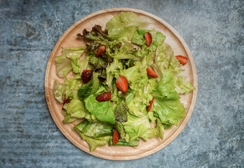 Top view Green salad with strawberries on wooden plate.