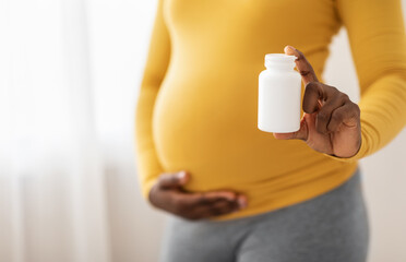 Closeup of black pregnant woman holding white jar with pills