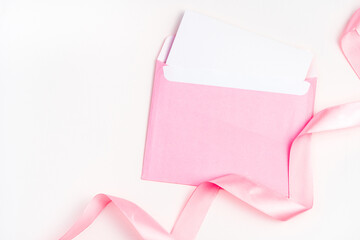 Pink envelope and satin ribbon on a light background. Top view with space to copy. Concept of holiday backgrounds.