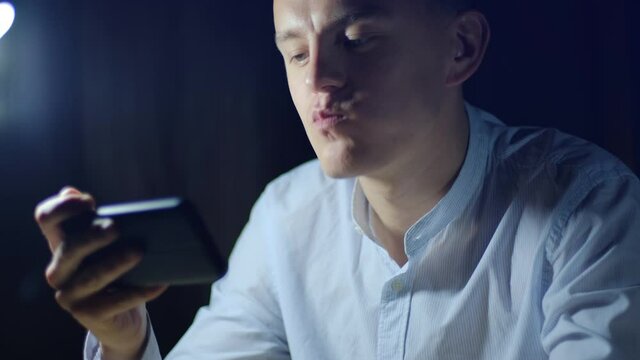 Young man watching video on smartphone and eating chips