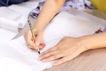 Obraz na płótnie Canvas Fashion designer's hands. Closeup of hands drafting a new sewing pattern on paper, tailor working with a pencil, ruler, fabric, tool. Textile industry, hobby, workspace. Creation process. Drawing