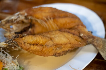 Close up of deep fried fish with fish sauce on the white plate.