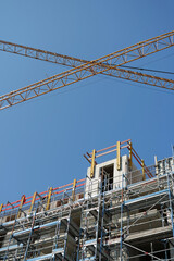 View of the top of a scaffolded new construction site with two yellow tower cranes crossing in front of the clear blue sky