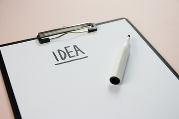 Conceptual photo. A clipboard on a beige background, sheet a4 on which the word idea is written with marker.
