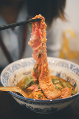 Lifting a slice of a premium medium raw Wagyu beef by using chopsticks from Thai noodle bowl