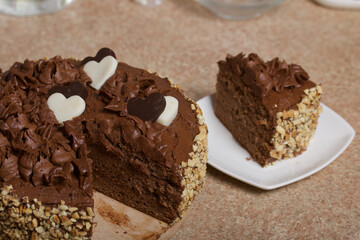 Chocolate cake with cream and peanuts. Decorated with chocolate hearts. On pine boards.