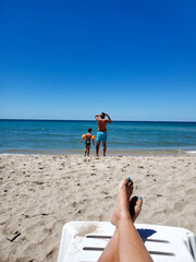 tanned legs on a sun lounger enjoying a beach holiday watching your child and husband.