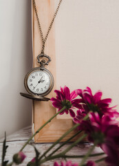 old round vintage watch on a chain among flowers in the interior