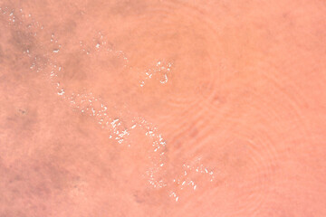 Fototapeta premium The natural surface of the salty pond is pale pink with a white path of will. Shooting from the air. Copy space.
