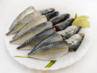 Cleaned and Ready to cook Fresh Fish Horse / Indian Mackerel Fish Decorated with herbs and Vegetables on a white plate.