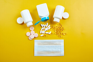 Flat lay of Medical face mask and pills, fish oil, vitamins on yellow background, coronavirus COVID-19 concept, Assorted pharmaceutical medicine pills, tablets and capsules, Immune booster.