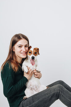 Young white woman hugs her jack russell terier puppy. Isolated on white background. Studio portrait. Owner and her dog posing together.