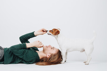 Young woman plays with her jack russell terrier dog isolated on white background. Girl lies down and looks up on her dog. Owner and dog have fun. Studio portrait.