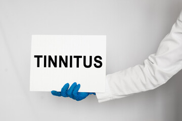 The doctor's blue - gloved hands show the word TINNITUS- . a gloved hand on a white background. Medical concept. the medicine