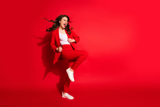 Full length profile photo of charming young girl crazy open mouth raise knee wear blazer pants footwear isolated red color background