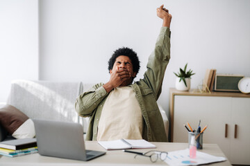 Tired black student yawning and stretching during his remote studies from home - obrazy, fototapety, plakaty