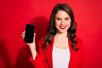 Photo of cute young lady hold demonstrate telephone screen empty space wear jacket isolated red color background