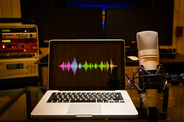 condenser microphone and colorful waveform on laptop computer display in recording, broadcasting studio background. audio recording, voice actor or podcasting concept