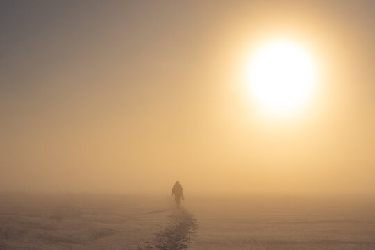 Winter picture. The man goes away in the snow. The image is blurred because of the snowfall. Cold yellow sun. Sad picture. Parting. Loneliness.