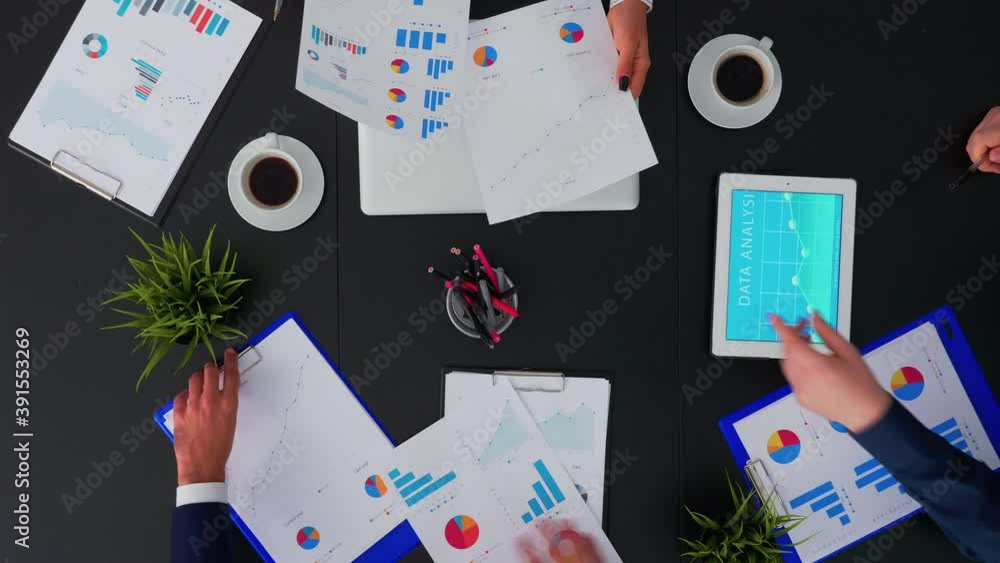 Poster top view of fast forward shot of people brainstorming financial statistics graphs planning next proj