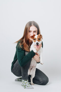 Young white woman hugs her jack russell terier puppy. Isolated on white background. Studio portrait. Owner and her dog posing together.
