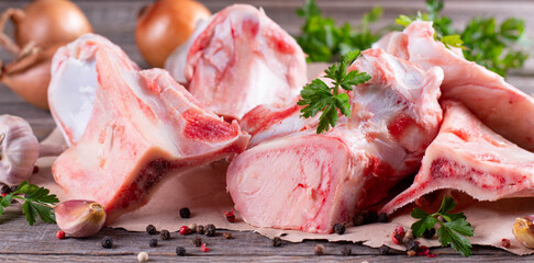 Raw beef bone for making broth on wooden background with vegetables and herbs. Banner