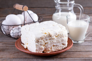 Food and eating concept - close up of cottage cheese, jug of milk, a glass of milk and chicken eggs on wooden table