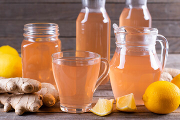 Kombucha or cider fermented drink. Cold tea beverage with beneficial bacteria, ginger, lemon on wooden table. For healthy nutrition.
