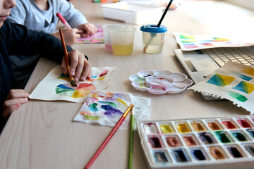 Children painting pictures with watercolor paints during art lesson. Pupils are concentrating on drawing with brush. Watercolor color wheel and palette. Color theory beginner hobby lessons