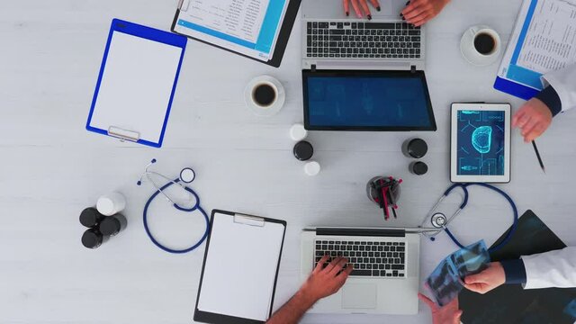 Top view of doctor explaining to resident physician patient problems using tablet and x-ray sitting at desk with stethoscope and digital device all around on copy space, flat lay.