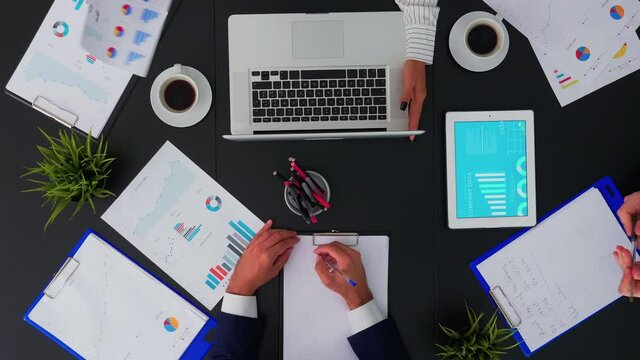 Directly above shot of businesspeople sitting at office desk and discussing financial documents using digital devices. Teamworkers planning in conference room on copy space, flat lay concept.