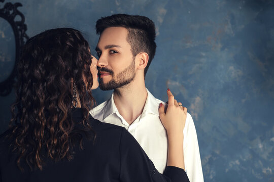 Gorgeous Glamour Couple Hugs And Kissing. Elegant Man With Trendy Beard And Smirk Face. Handsome Male With Confident Look And Stylish Hairstyle In Old Apartment Photostudio Room.