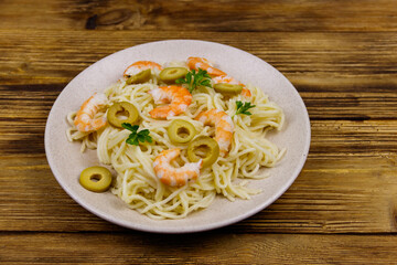 Spaghetti pasta with prawns, green olives and parsley on wooden table