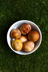Top view of brown Easter eggs, colored traditionally with onion peels, in a bowl on green spring grass with copy space on top and on the bottom