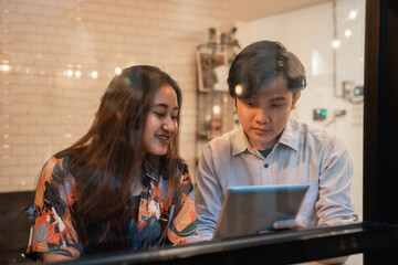 Asian young couples enjoy looking at the tablet PC screen together while sitting in a coffee shop