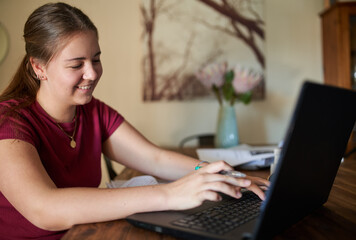 Teenager girl studying online at home looking at laptop during online class