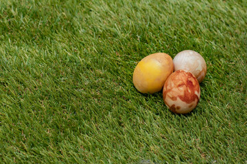 Three brown Easter eggs, colored traditionally with onion peels, in spring grass with text space on one side