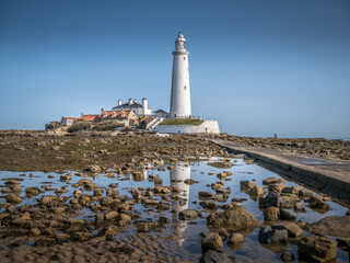 St. Mary's Lighthouse reflecting in rock pools on a bright day from the the causeway at Whitley...