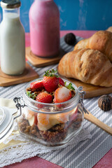 glass container with granola, strawberries, mandarin orange, croissant bread with almond milk