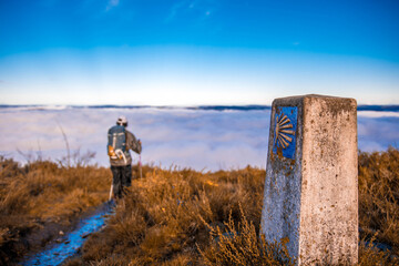 Peregrino recorriendo el camino primitivo de santiago sobre un mar de nubes y con la concha en...