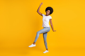 Full length body size photo of cheerful girl with black skin listening melody dancing with orange earphones smiling laughing isolated on bright yellow color background