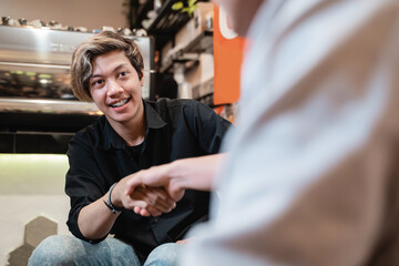 asian young man shake hands with partner when sitting on sofa in coffee shop