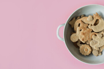 Holidays spirit concept: gingerbread or season biscuits shaped as fir tree, forest animals, man, stars and hearts on white china bowl. Fat lay. Top view with copy space on pastel pink background.