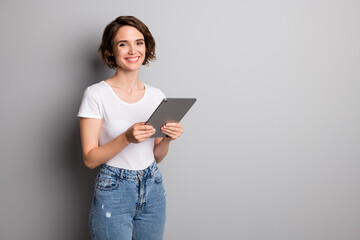 Photo of cheerful positive toothy smile young woman hold computer tablet wear casual outfit isolated over grey color background
